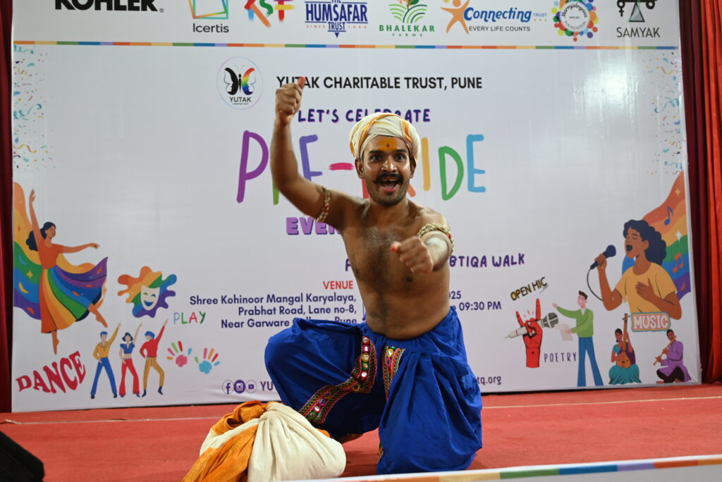 Man wearing blue dhoti & white turban, giving a vibrant performance on stage, as part of pre-pride talent-show activity